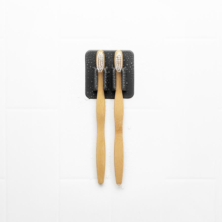 black silicone toothbrush holder with toothbrushes in it on a white tile background.