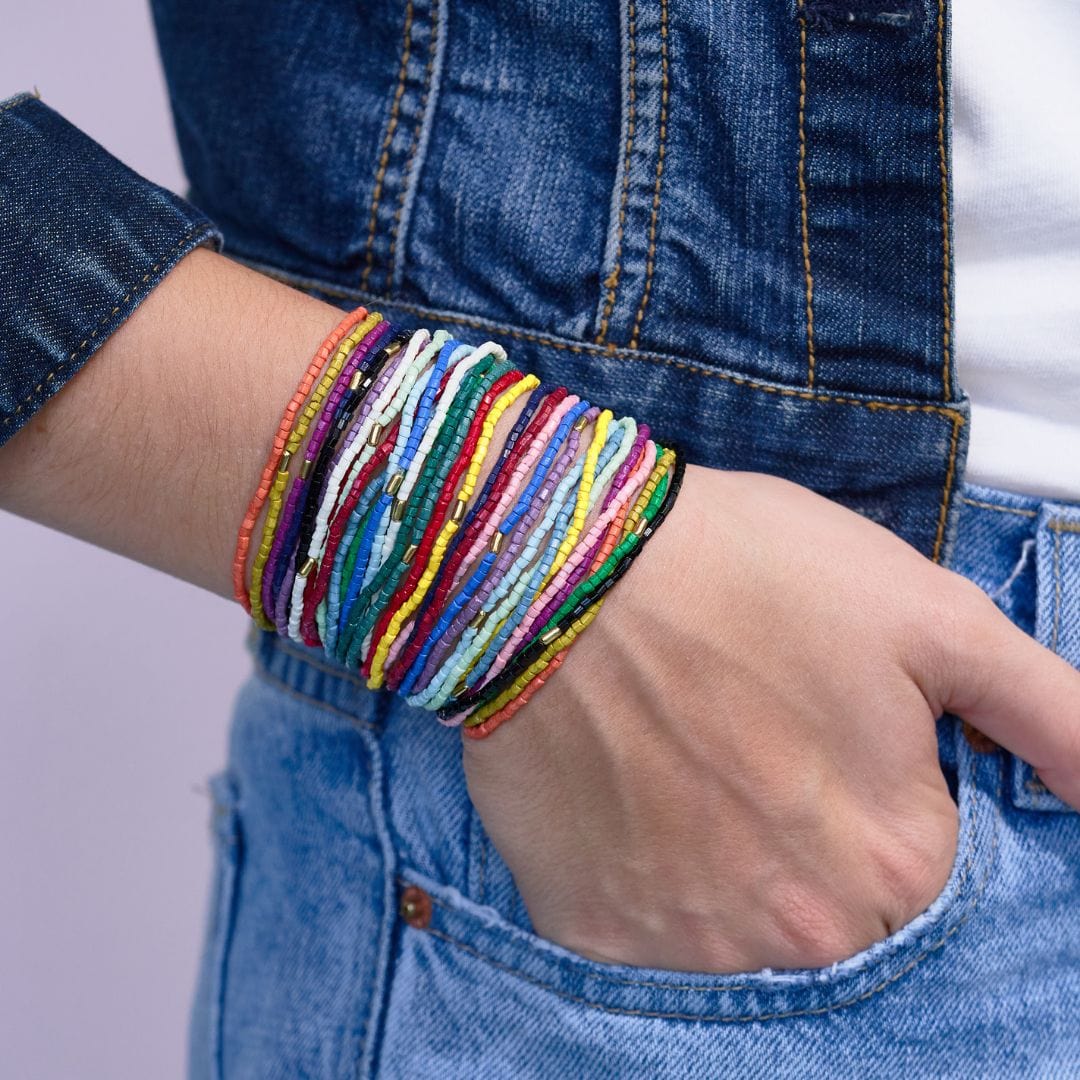 person wearing multicolored beaded bracelets with a denim jacket and jeans