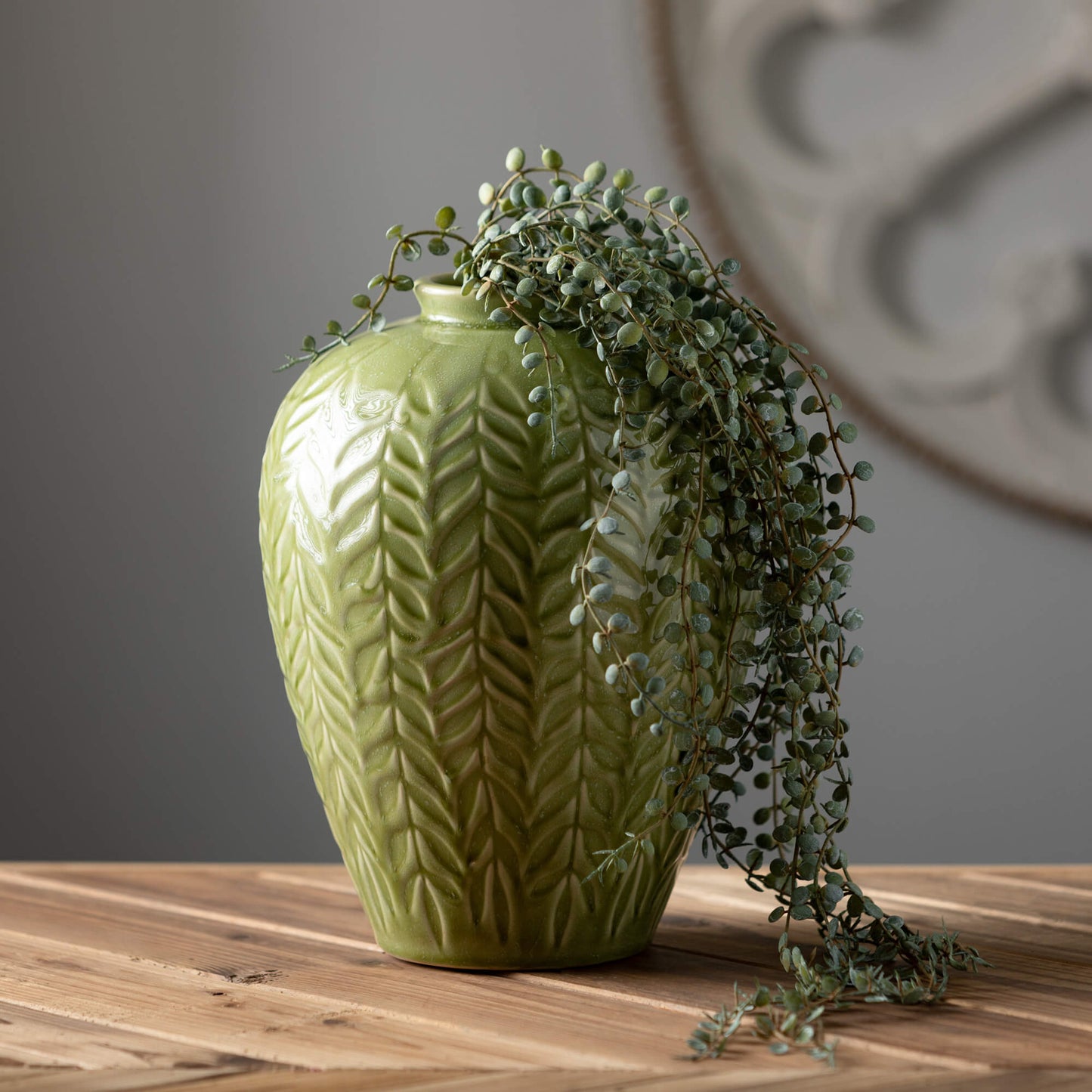 Textured Leaf Vase with trailing greenery in it set on a wooden table