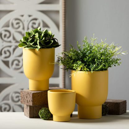 3 sizes of yellow planters arranged on a table with greenery, brinks, and moss orbs.