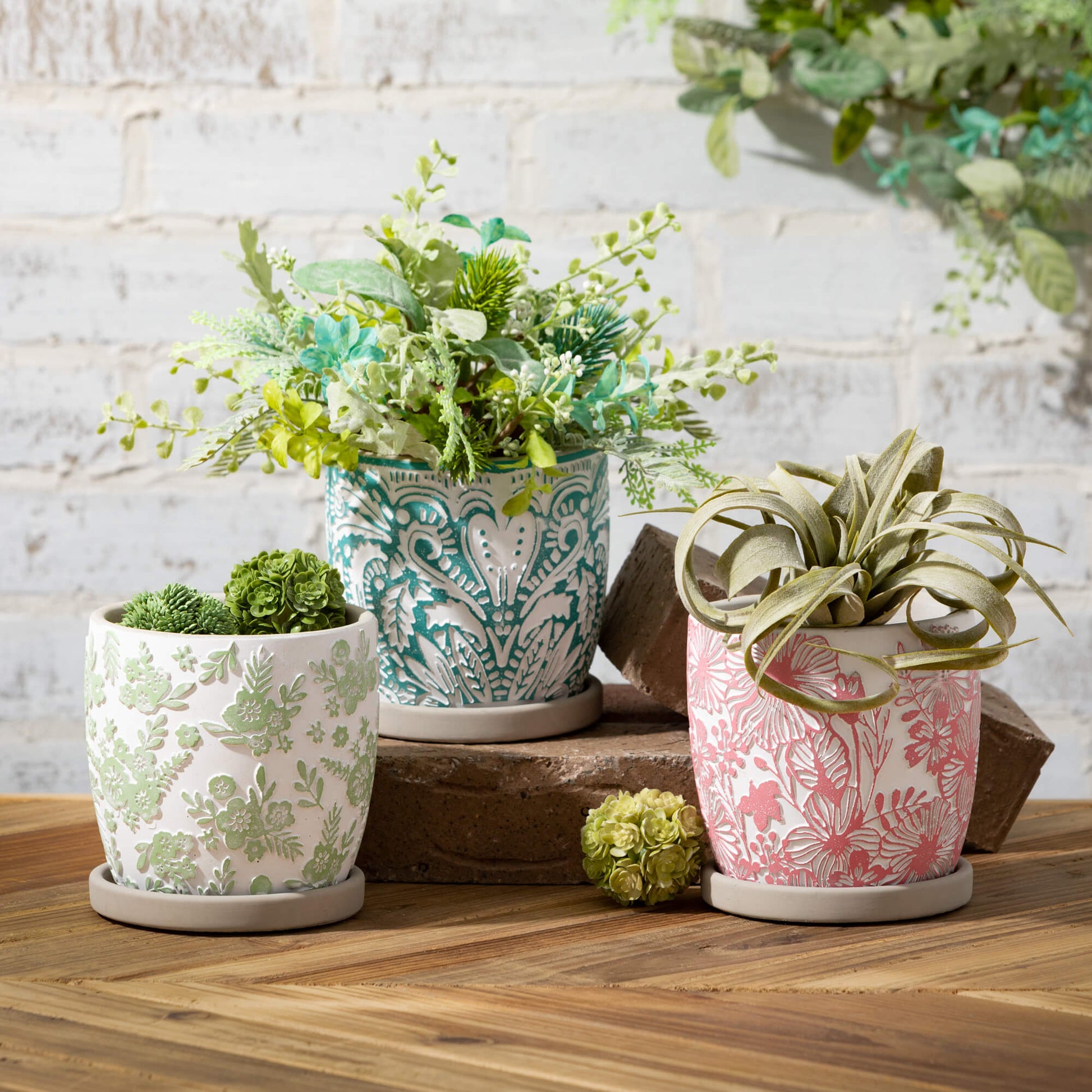 3 colors of cement pots filled with greenery arranged on a table with bricj risers.