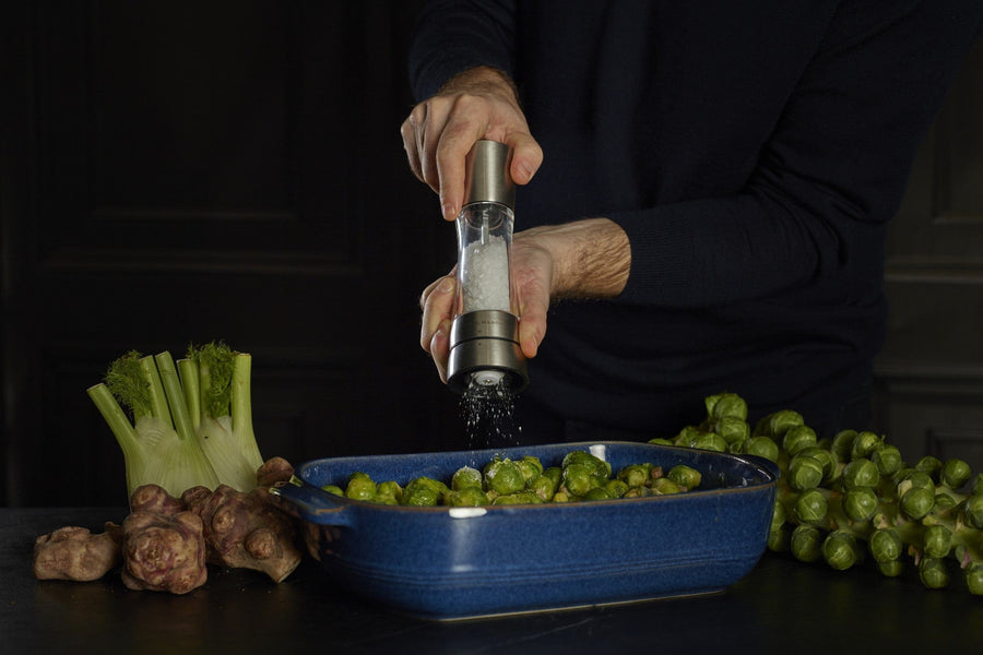 hands holding salt mill over a dish filled with Brussel sprouts.