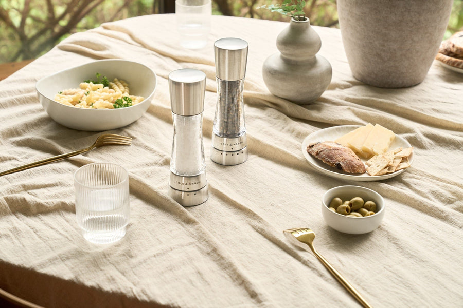 salt and pepper mills set on a table arranged with bowls and plates of food, a glass, and vases.