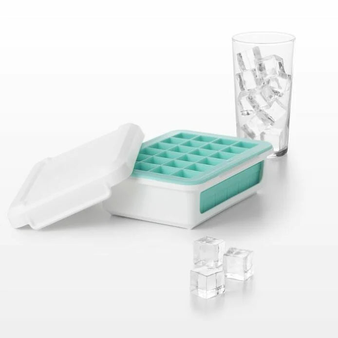 ice cube tray with ice cube set around it and a glass behind it