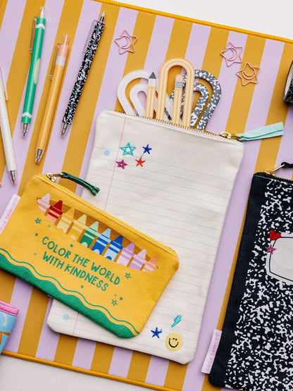 A styled flat-lay of pastel-colored zippered pencil pouches on a yellow and lavender striped background, surrounded by stationery items like pens, paper clips, and pencils.