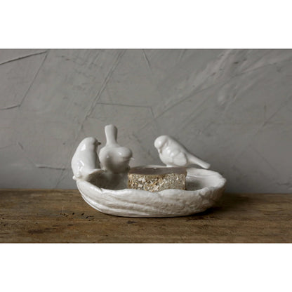 Decorative ceramic dish with birds perched on the rim and filled with bird seed set on a wooden surface and gray background