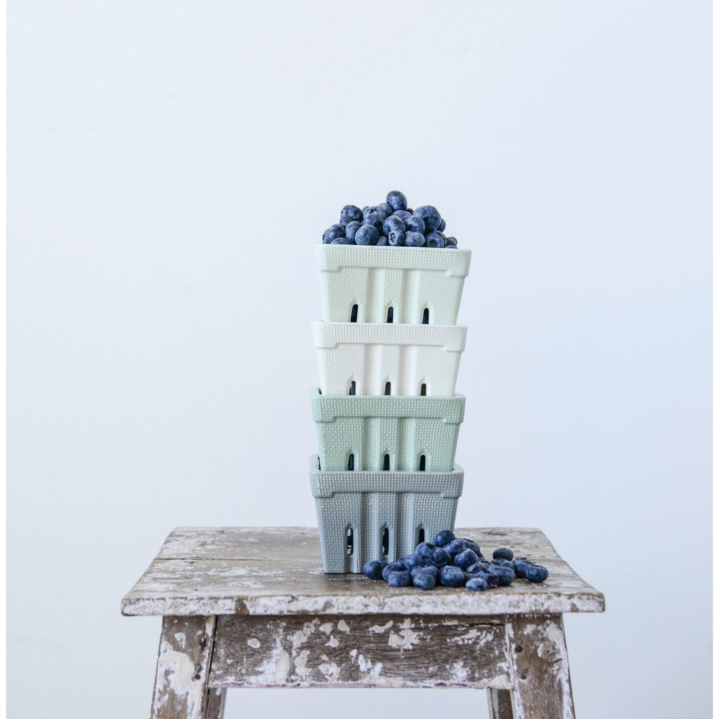 Four colors of stone wear berry baskets stacked and arranged with blueberries.
