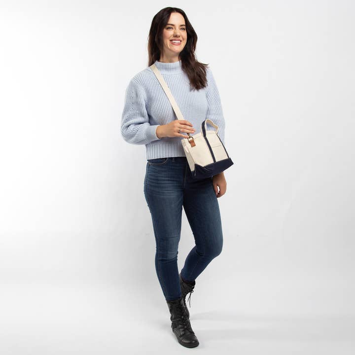 person wearing jeans and a light blue sweater with off-white tote with navy trim worn as a crossbody bag