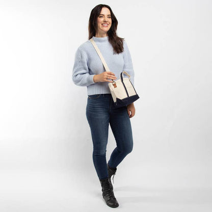 person wearing jeans and a light blue sweater with off-white tote with navy trim worn as a crossbody bag