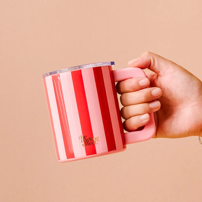 Hand holding a red and pink striped mug on a beige background