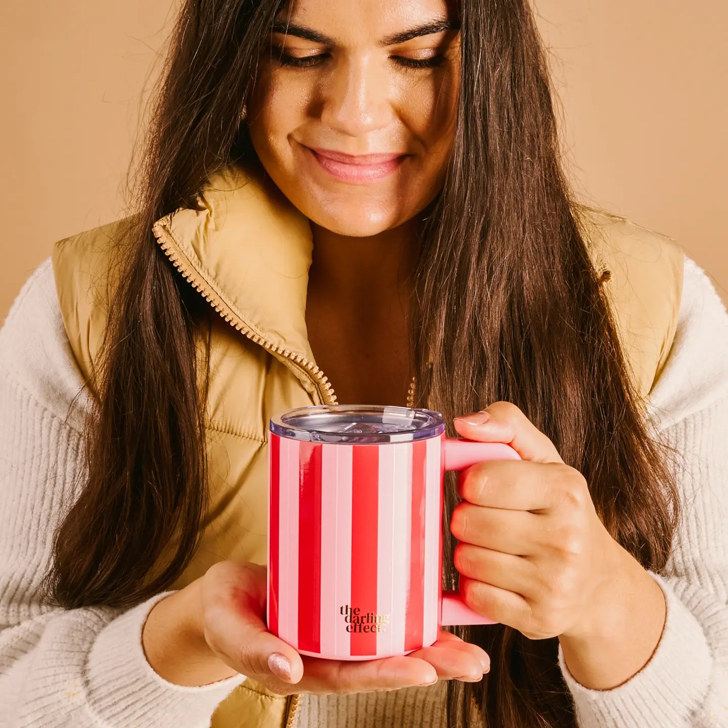 person holding a red and pink striped mug on a beige background