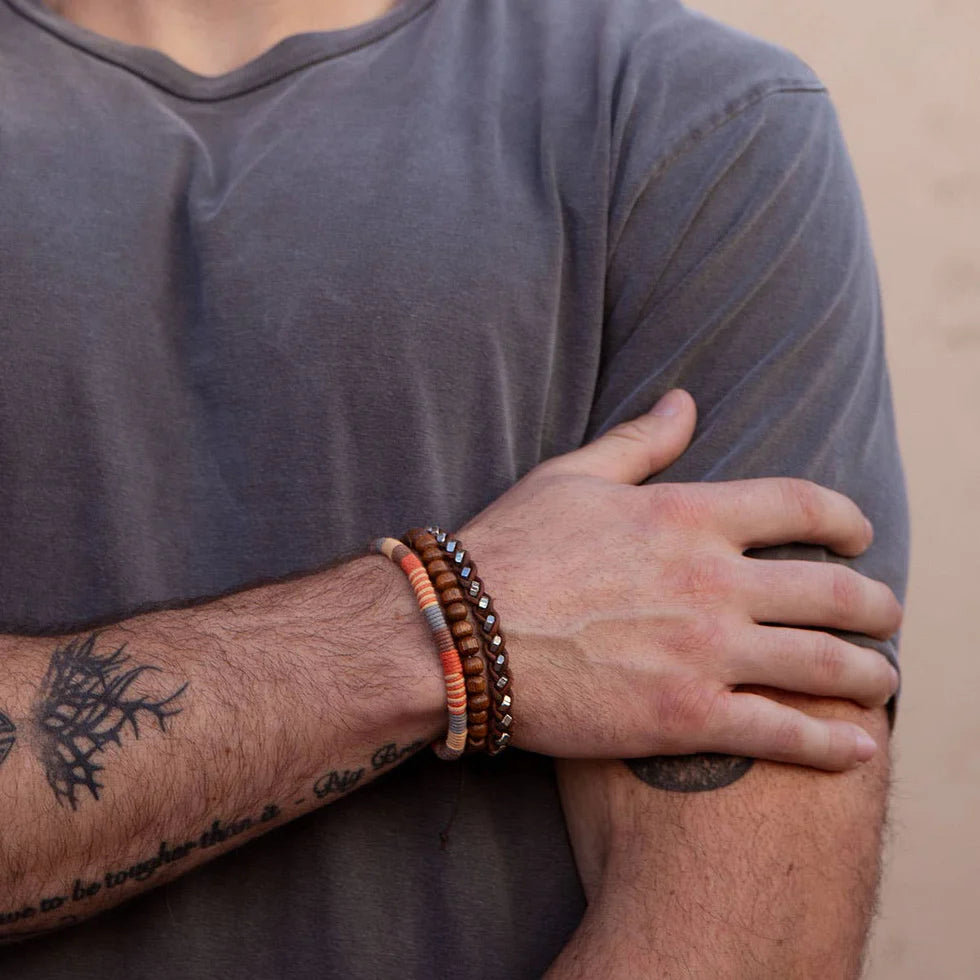 Person wearing multiple bracelets on a tattooed arm with a neutral background