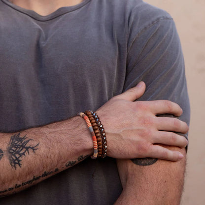 Person wearing multiple bracelets on a tattooed arm with a neutral background