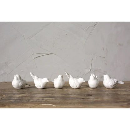 6 assorted white ceramic birds arranged on a wooden table with a plaster background.