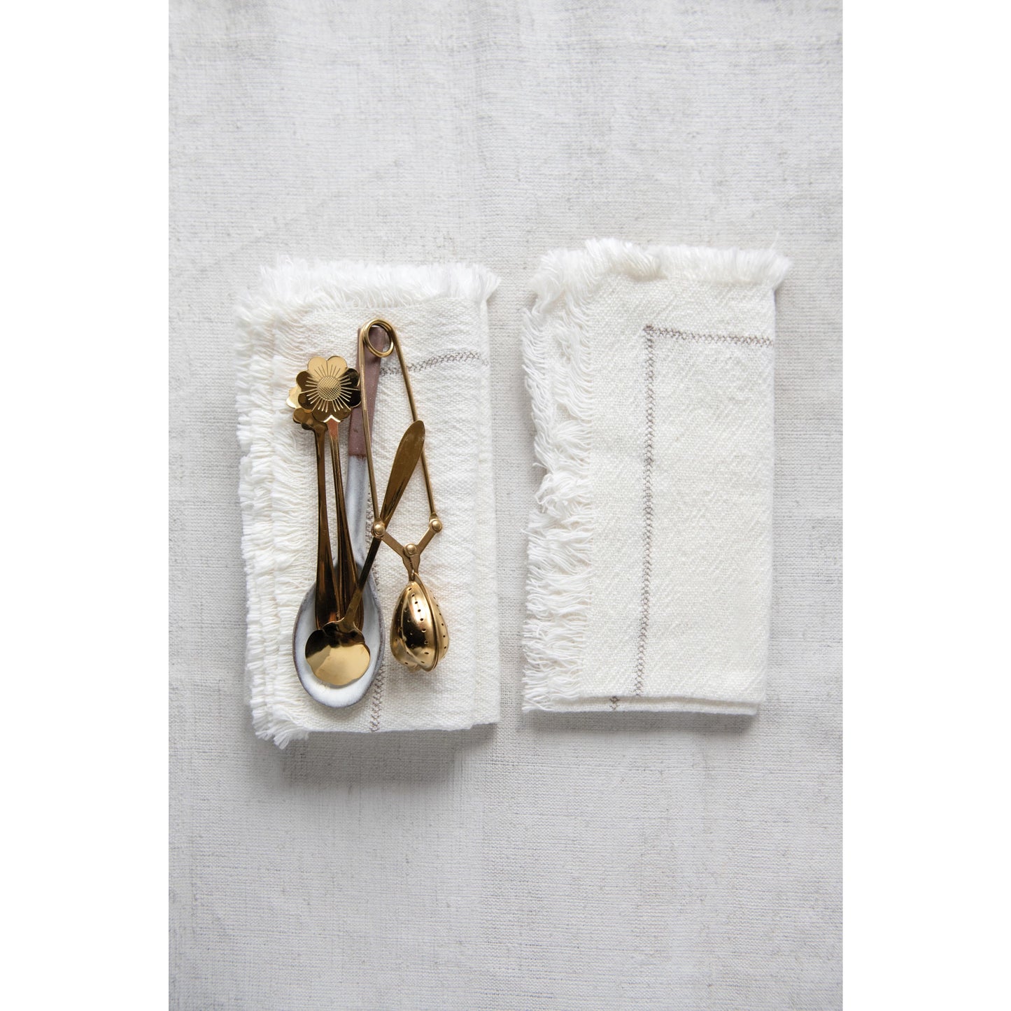 stack of white napkins with gold utensils placed on it and another napkin set set to it.
