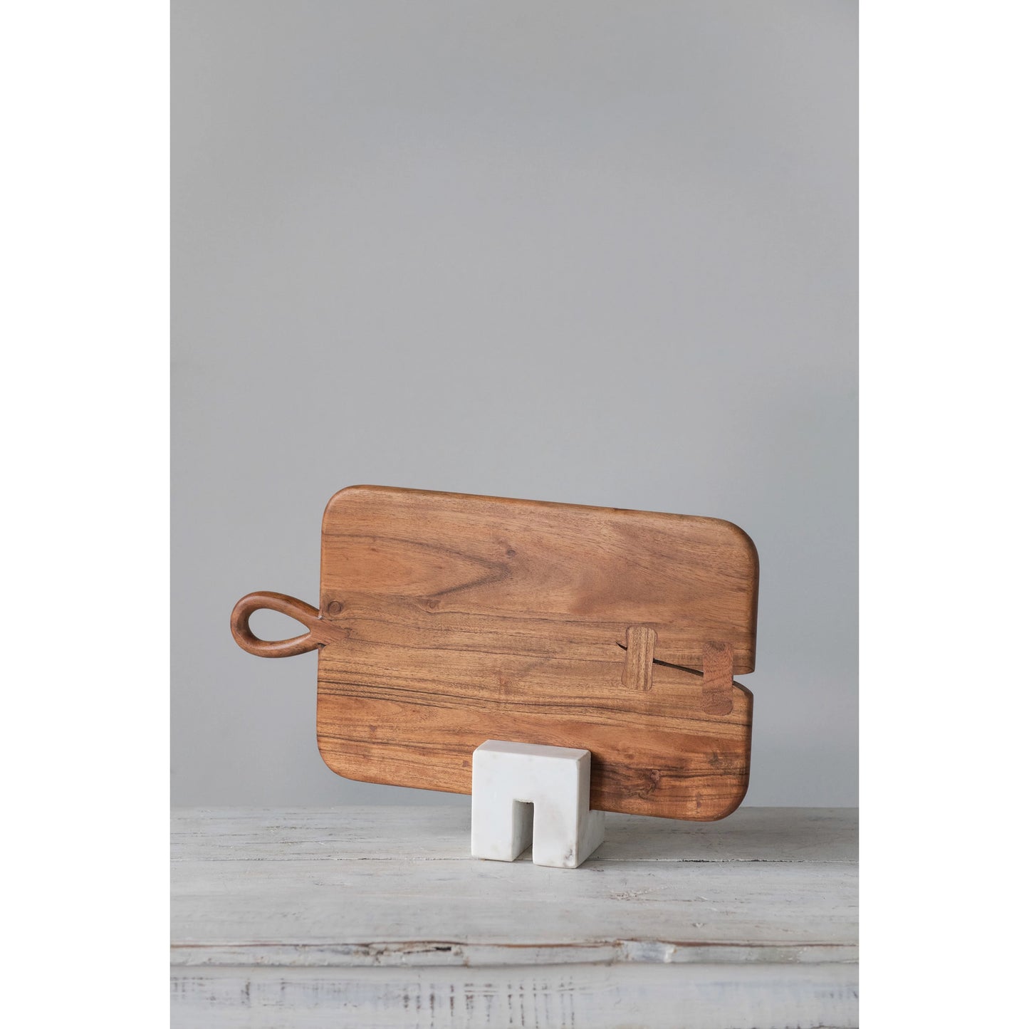 wood board with curved handle propped in a marble stand.