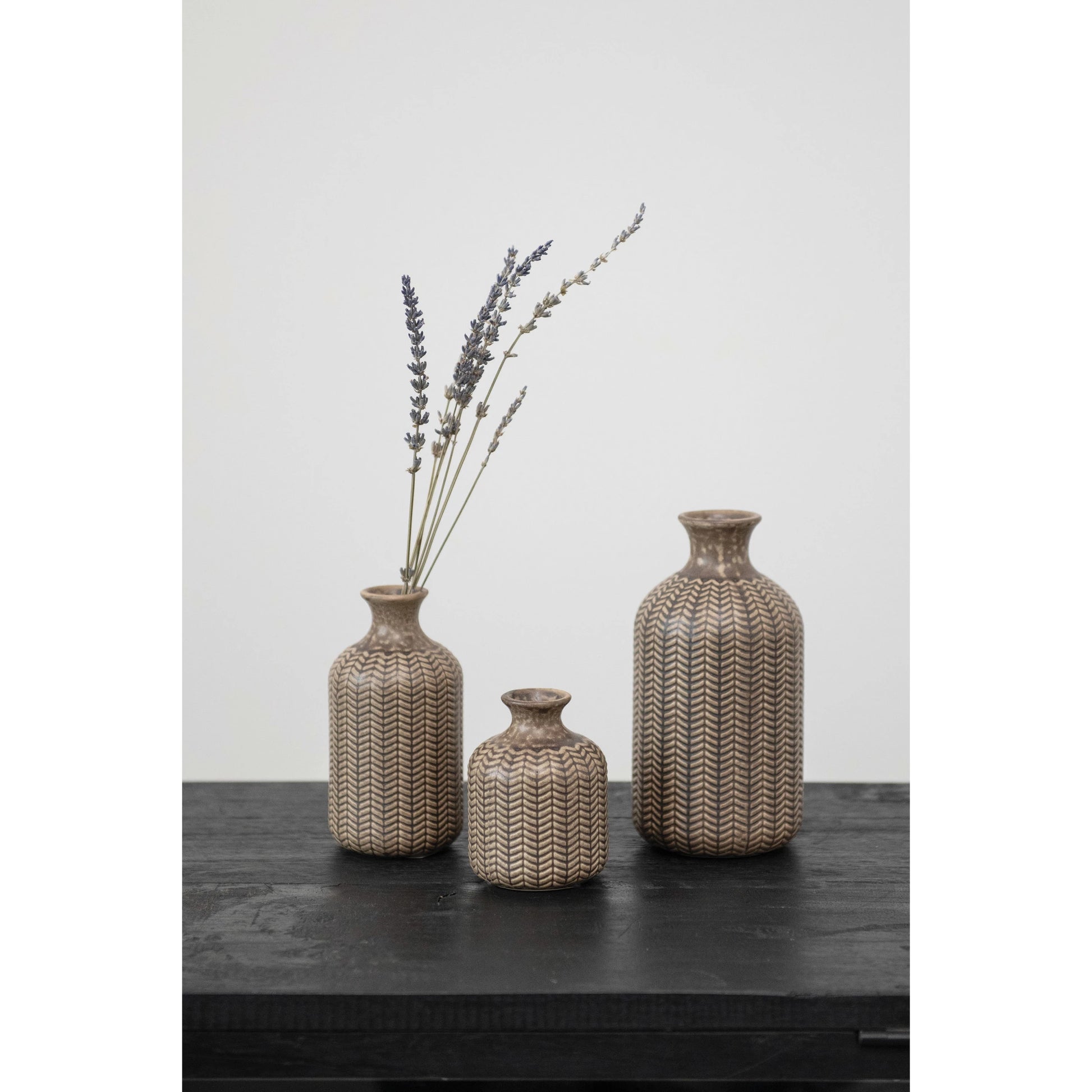 3 sizes of Embossed Stoneware Vases arranged on a black table, one vase has dried lavender in it.