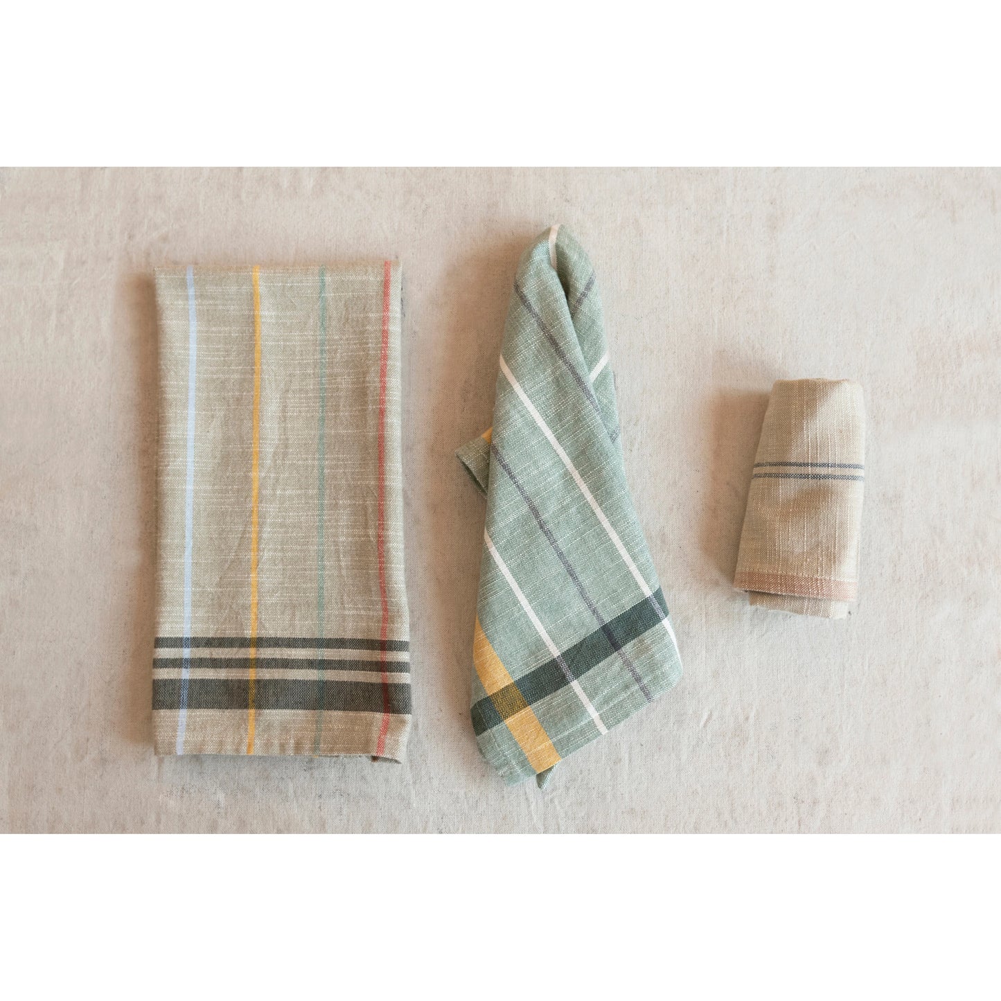 3 assorted striped towels folded or draped on a grey table.