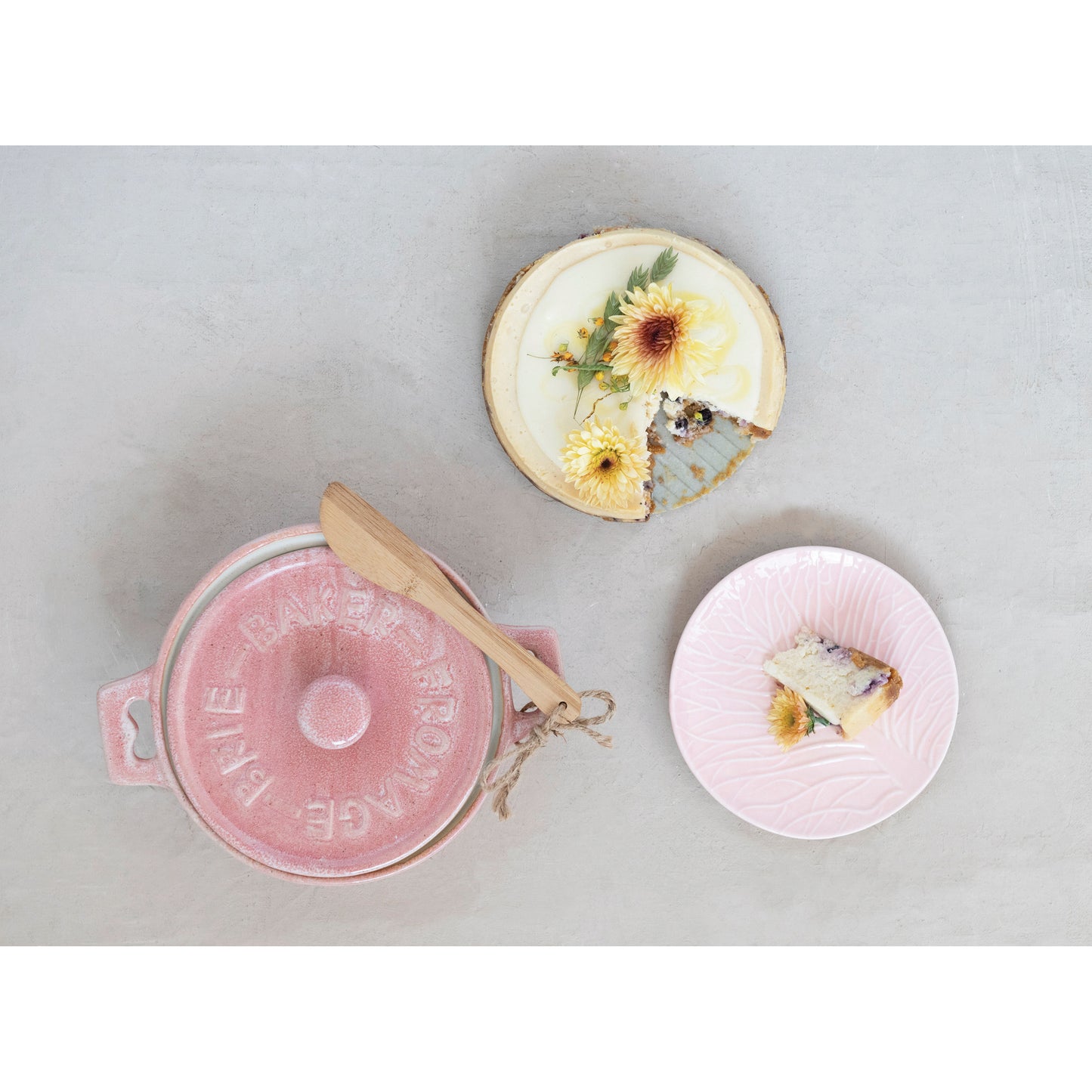 small pink ceramic baker with lid on it set next to a cheesecake and a piece of it on a plate
