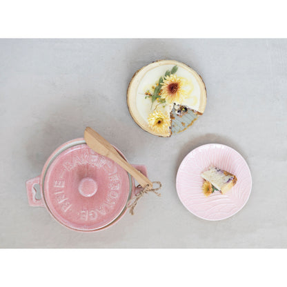 small pink ceramic baker with lid on it set next to a cheesecake and a piece of it on a plate