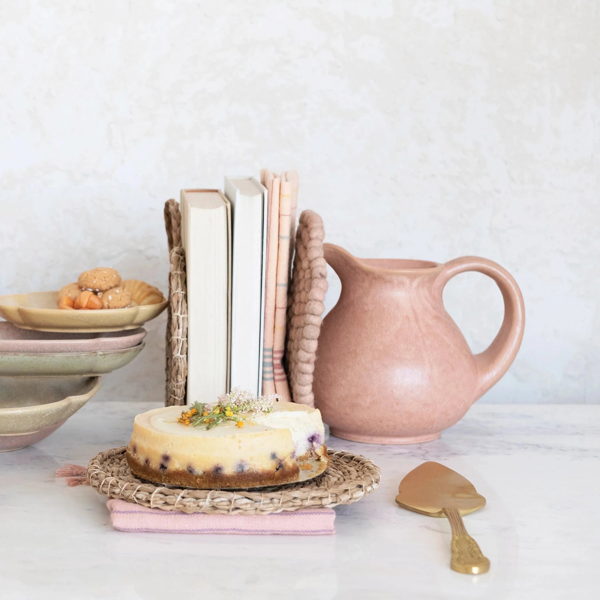 pink pitcher set on a countertop with books, plates, a cake, and cake server.