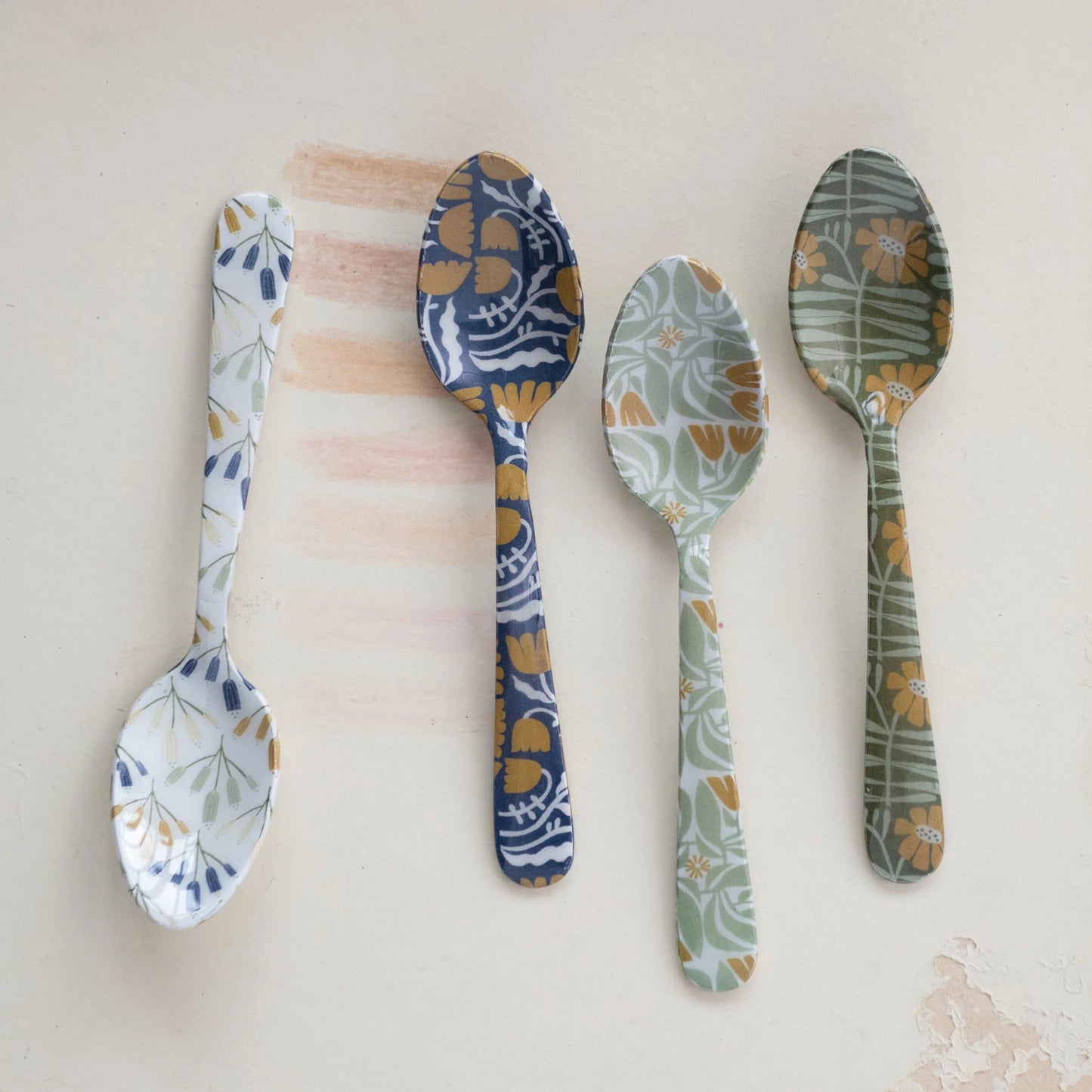 all four styles of enameled stainless steel spoon with flowers displayed against a light pink background