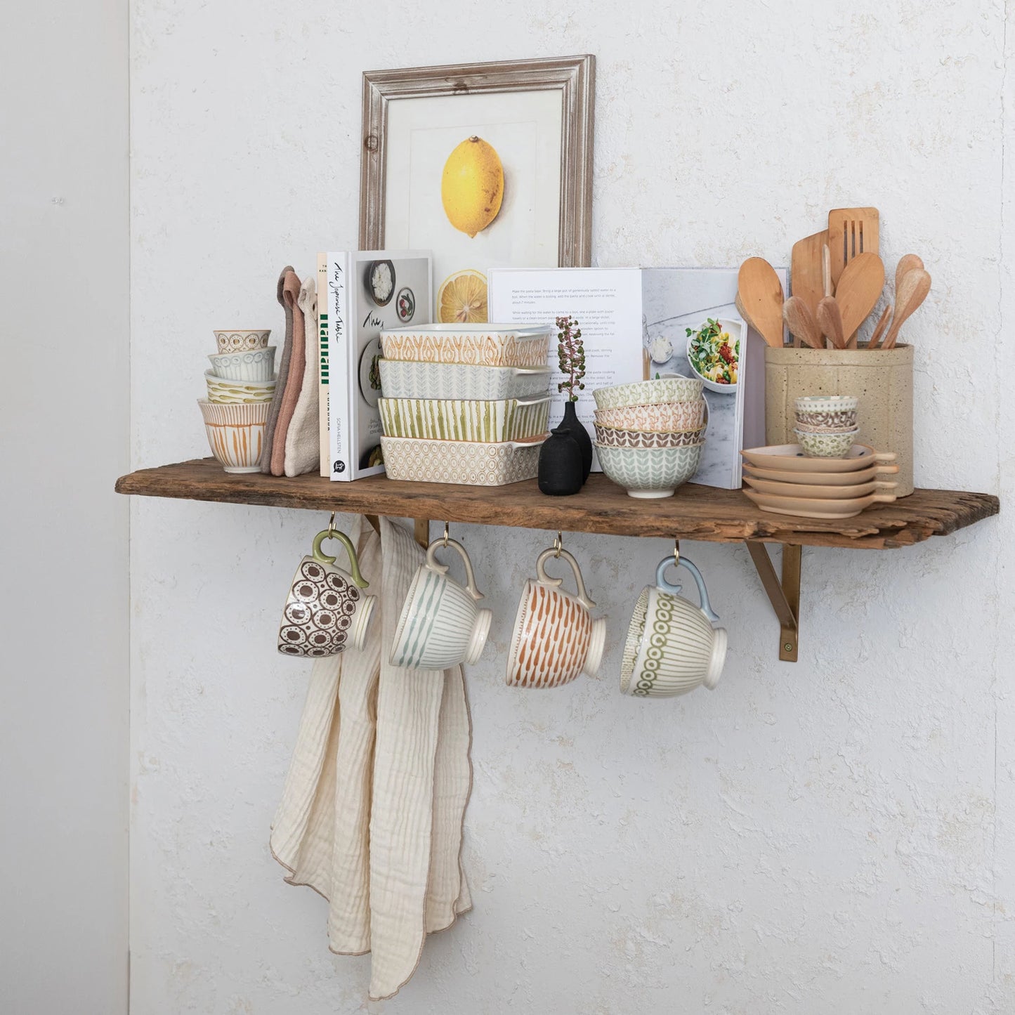 4 mugs hanging under a shelf filled with bowls, bakers, and books.