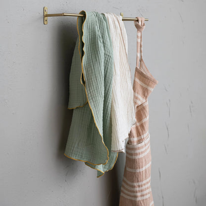 side view of gold metal rod mounted to grey wall with towels and an apron hanging on it.
