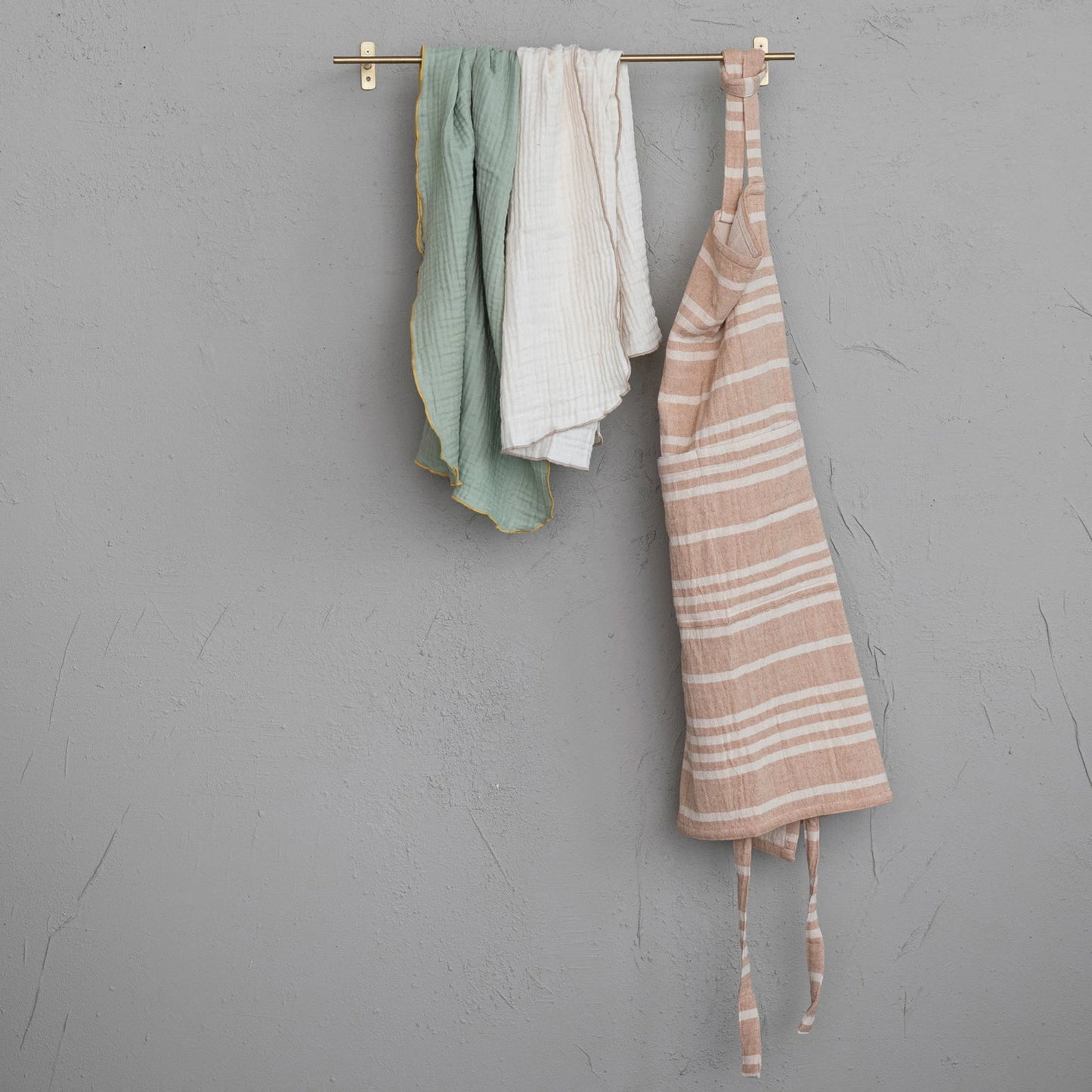 front view of gold metal rod mounted to grey wall with towels and an apron hanging on it.