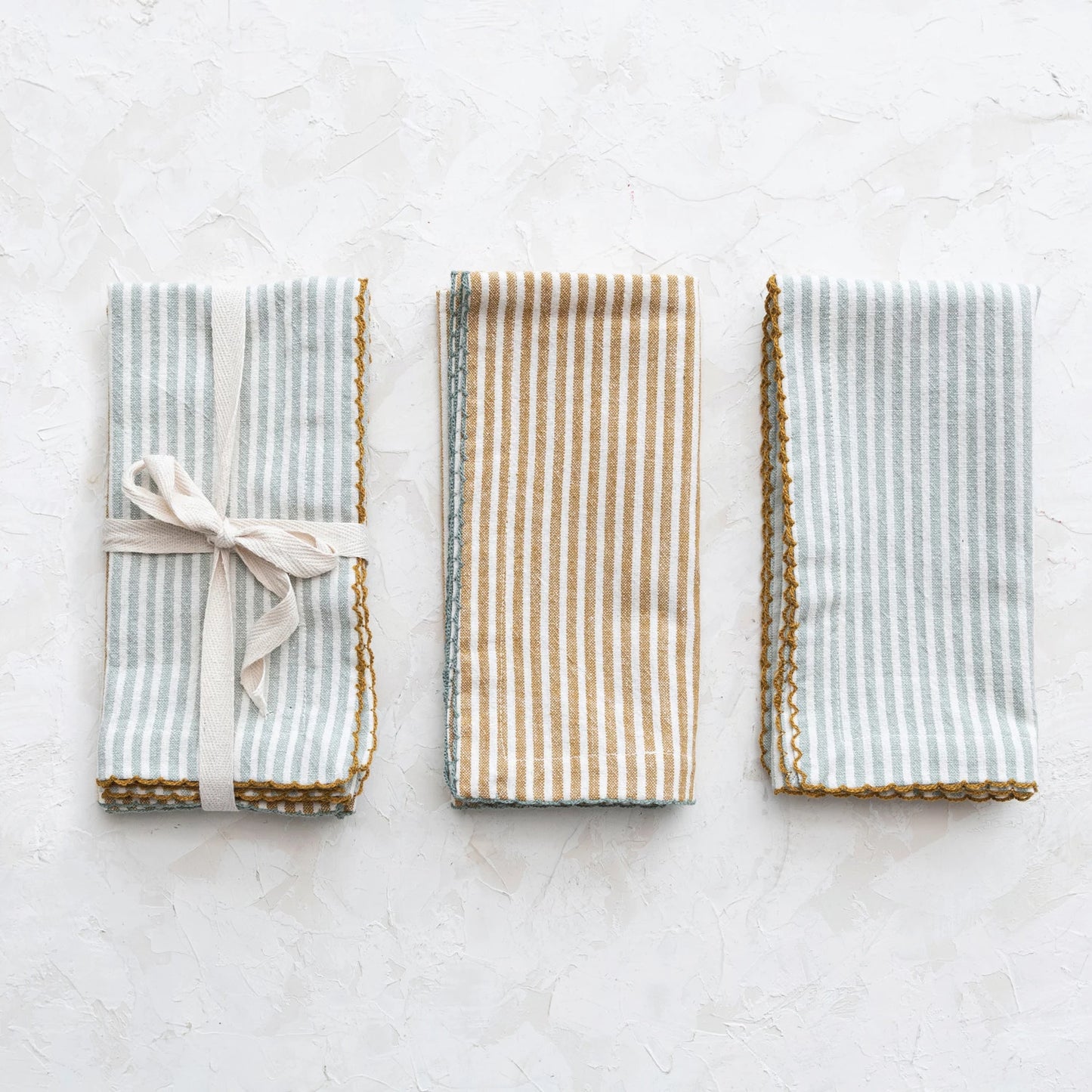 set of napkins folded and tied together with ribbon and 2 other napkins folded and set next to it on a grey surface.