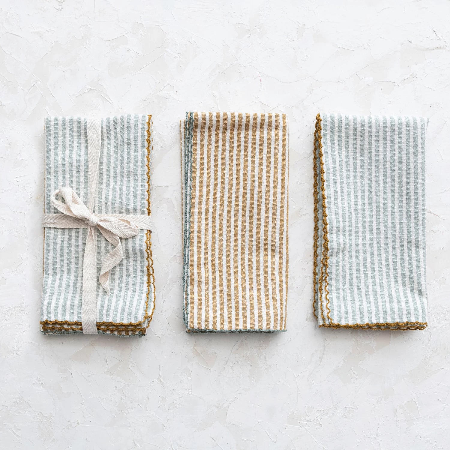 set of napkins folded and tied together with ribbon and 2 other napkins folded and set next to it on a grey surface.