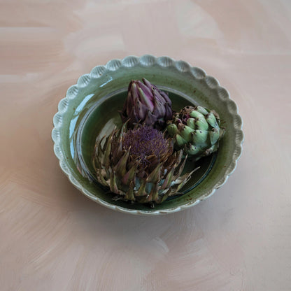 scalloped edge bowl filled with artichokes and set on a table.