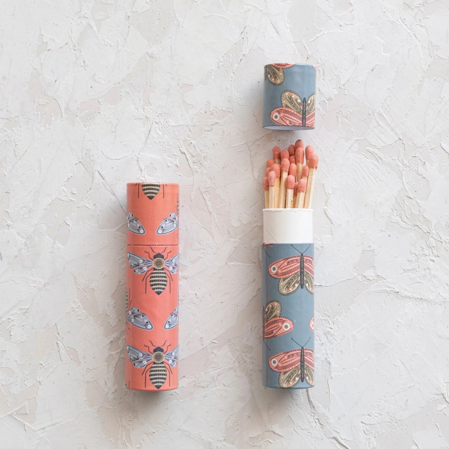 2 styles of match tubes laying on a plaster surface, one tube is open with matches coming out of it.