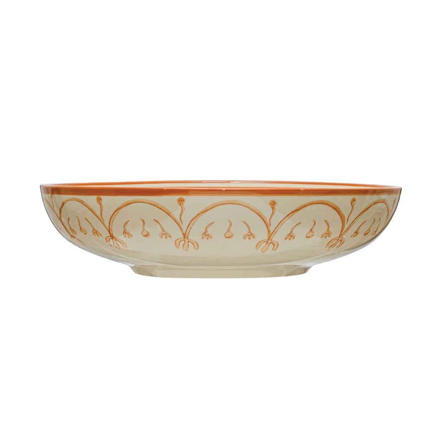 side view of cream colored bowl with orange swirled pattern.