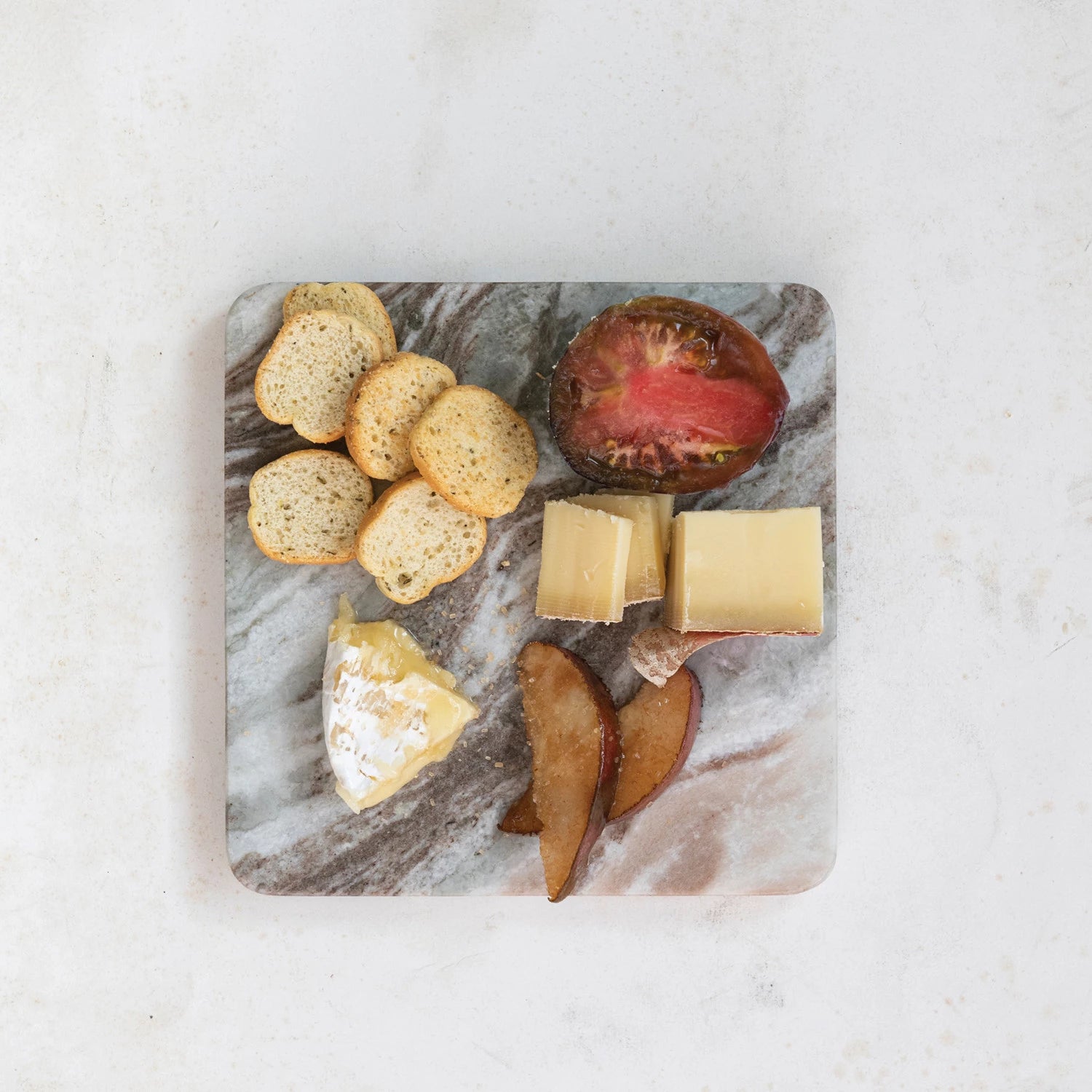 top view of marble with bread slices, cheese wedges, and fruits on it.
