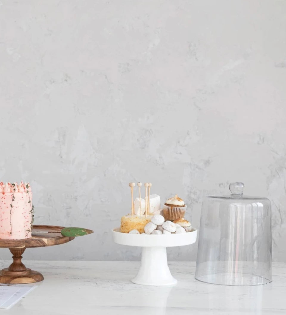 white pedestal with sweets on it and a glass cloche set next to it.