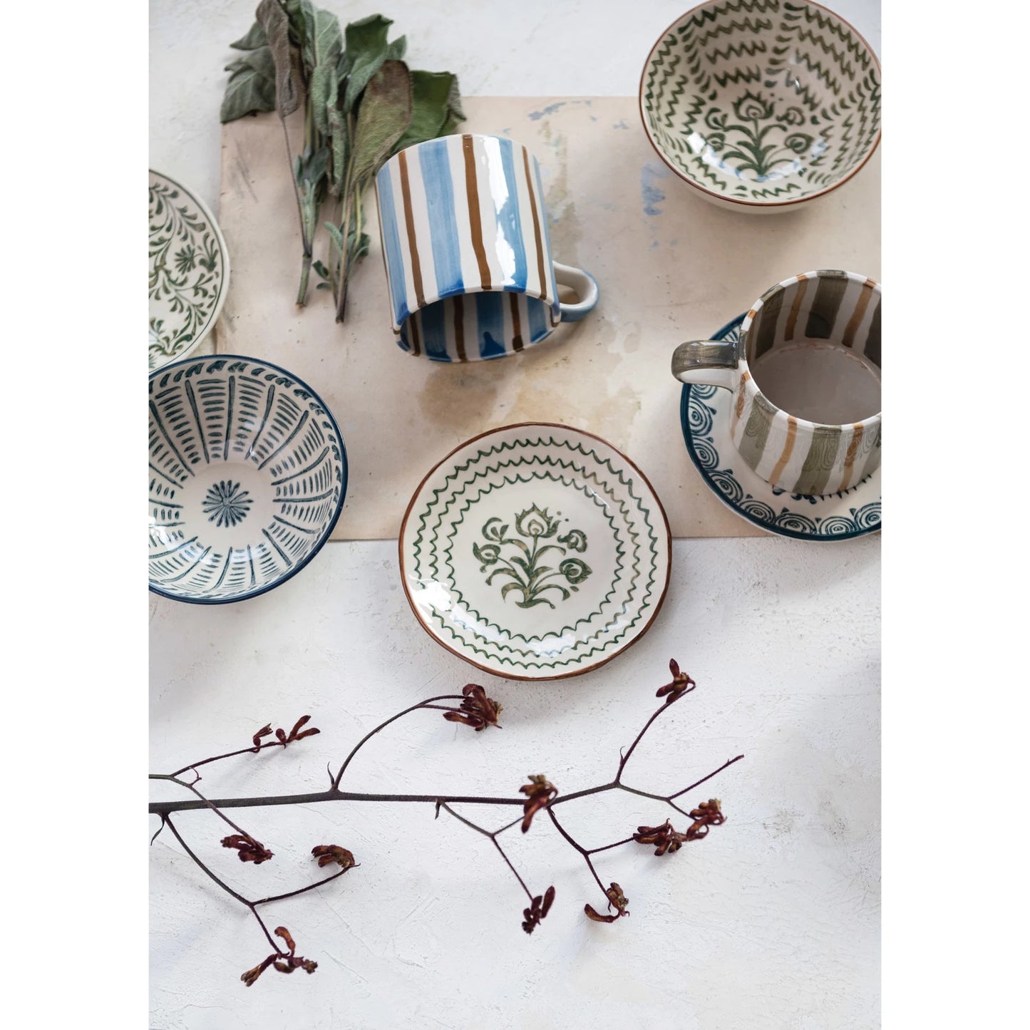 top view of table arranged with assorted petite plates, bowls and dried greenery.