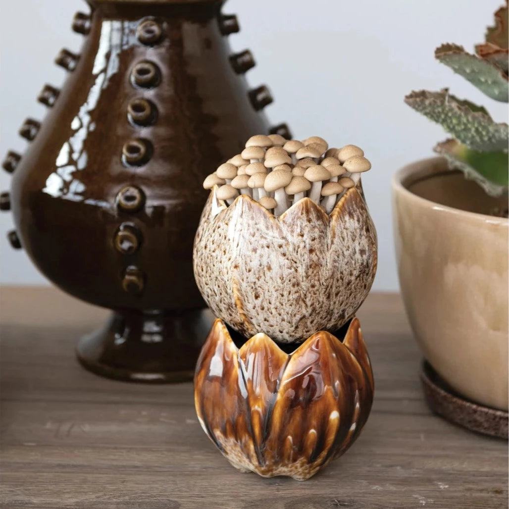 two stoneware flower shaped planters stacked and displayed next to vases filled with plants and greenery