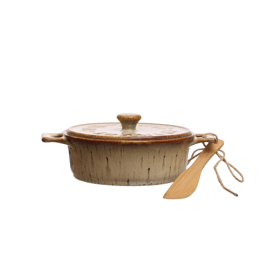 stoneware brie baker with tan and brown reactive glaze, a lid on it,  and a bamboo spreader tied to the handle.