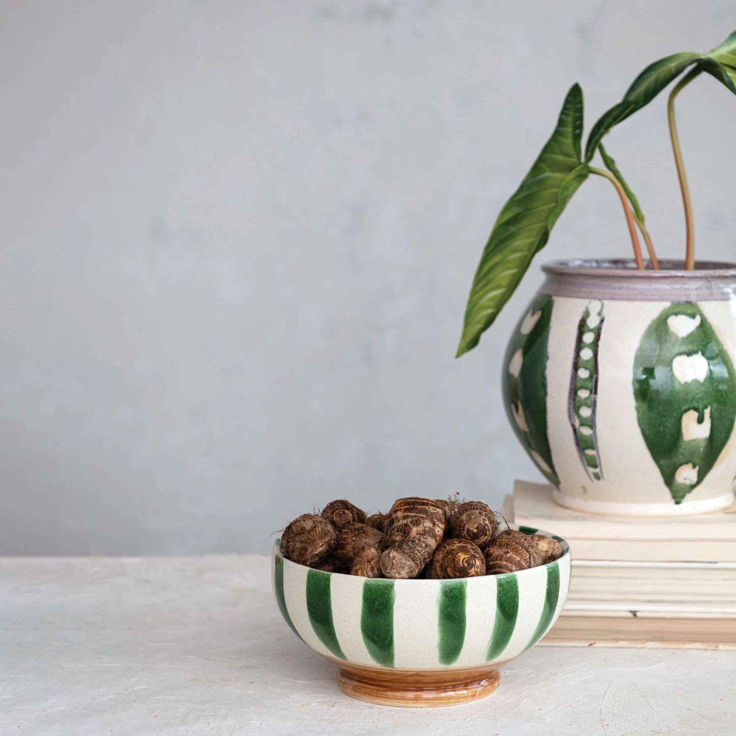 cream bowl with green stripes filled with tubers set on a table next to a plant.