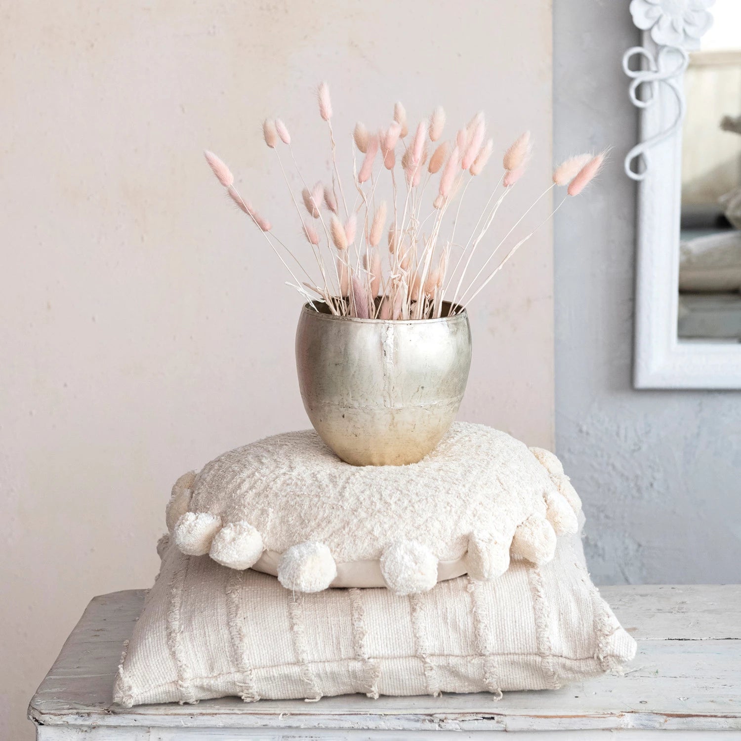 the large distressed pewter finish metal planter filled with dried grass and displayed stacked on two white pillows 