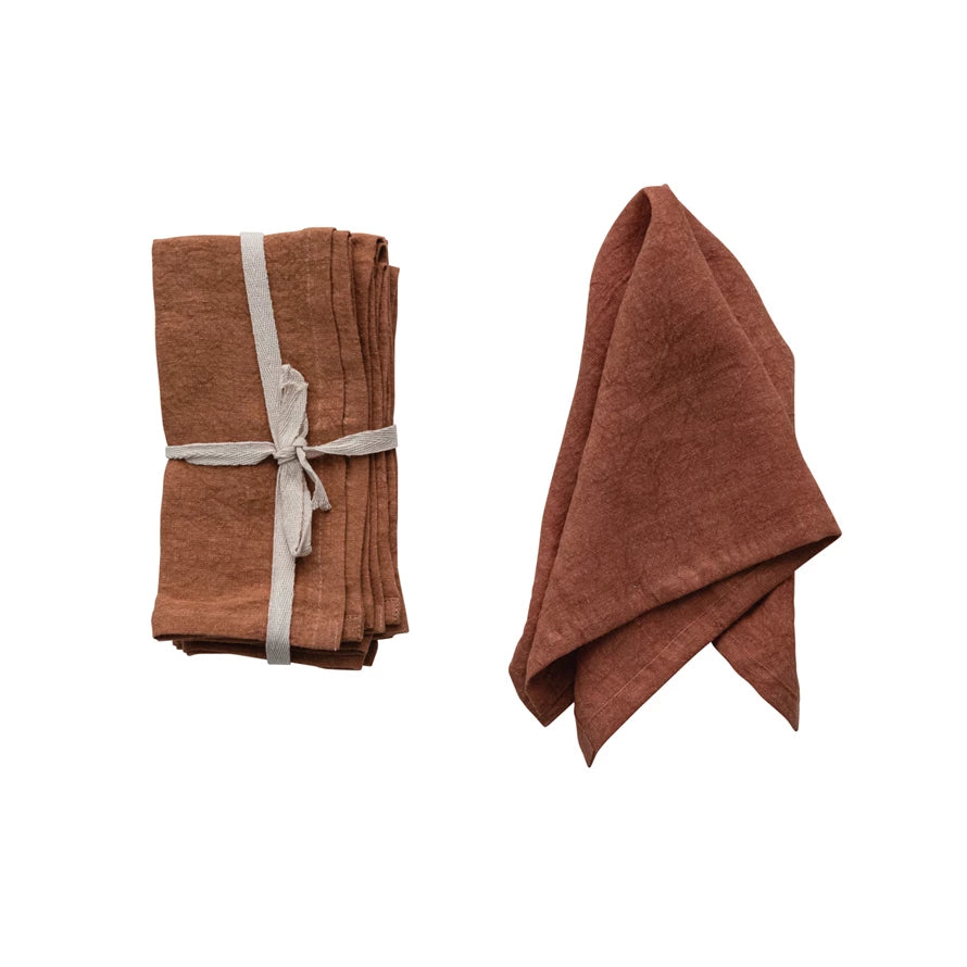 set of folded rust Stonewashed Linen Napkins tied with ribbon and one displayed draped over itself on a white background