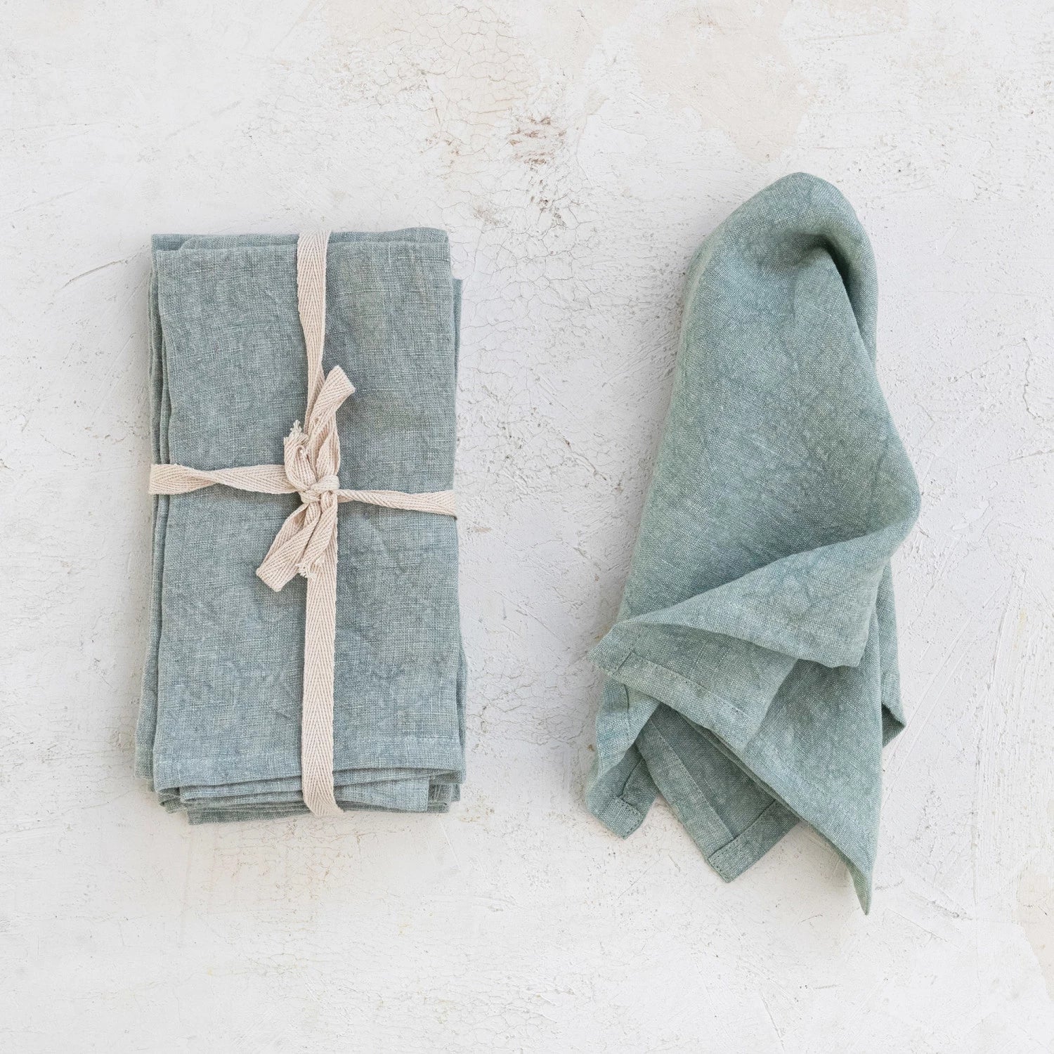 mint linen napkin draped next to a stack of napkins tied with a ribbon.