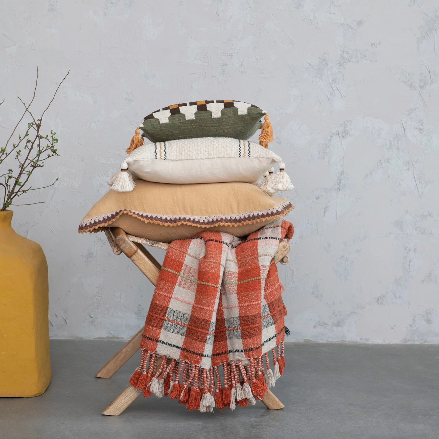 plaid Throw displayed on a wooden folding chair beneath three decorative pillows and next to a square yellow vase