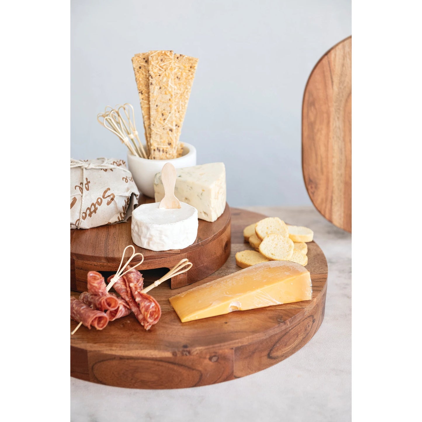 2 sizes of round wood boards stacked with cheeses and meats arranged on them.