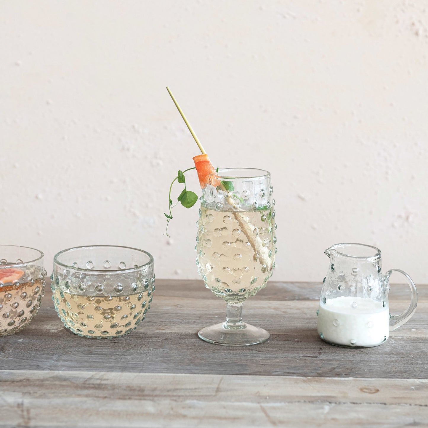 hobnail drinking glass filled with beverage and a garnish set on a table with other glassware 