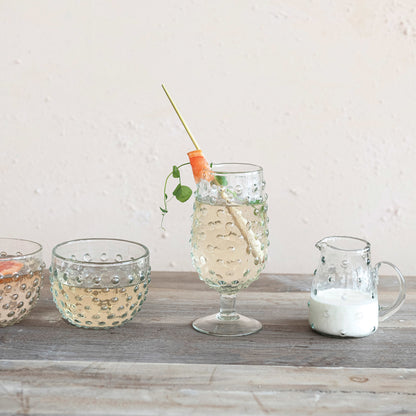 hobnail drinking glass filled with beverage and a garnish set on a table with other glassware 