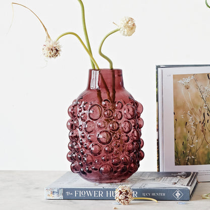 purple glass vase with raised dots filled with 3 onion stems and set on a book.