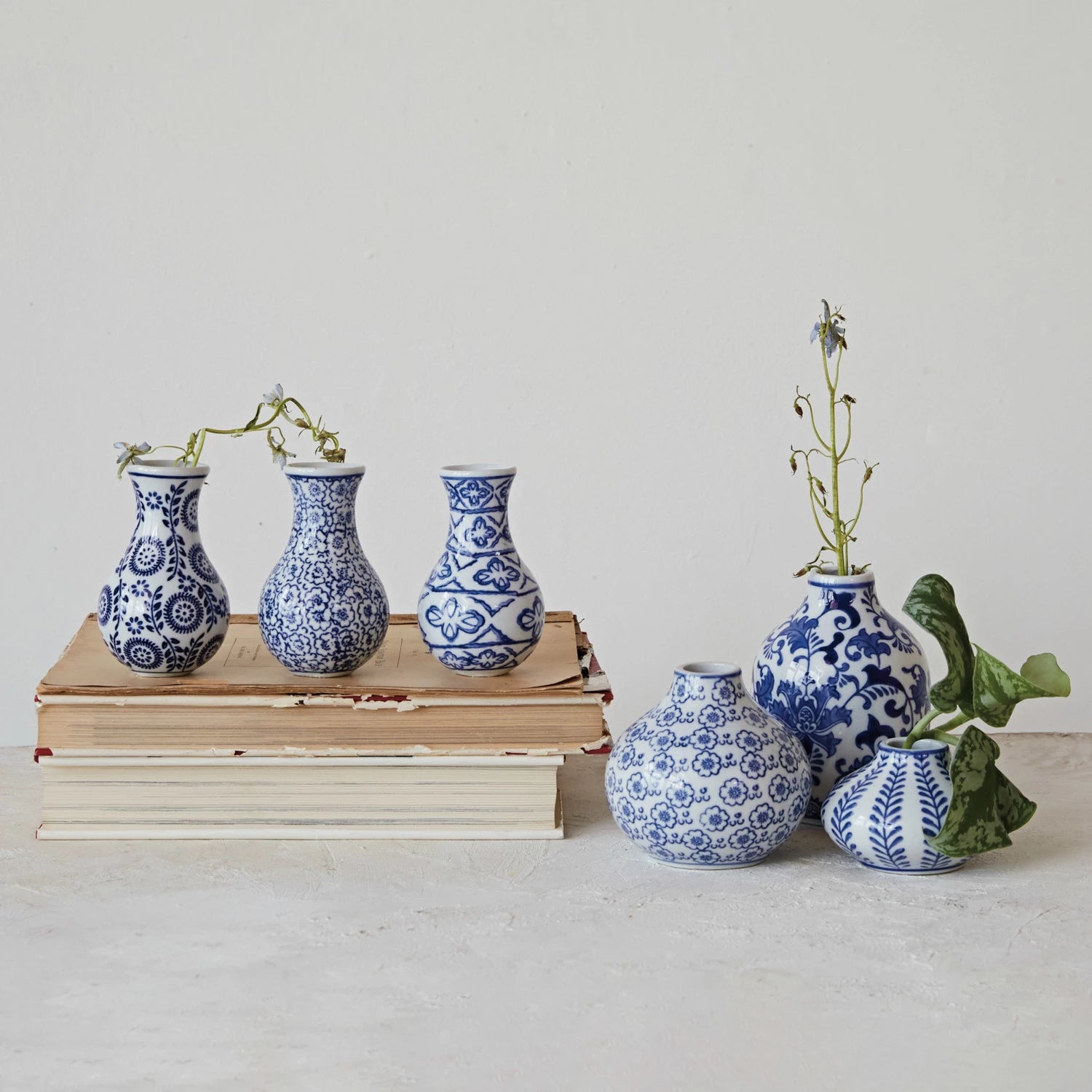 assorted blue and white vases arranged on a shelf with books and greenery.