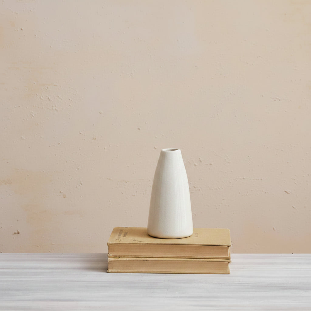 medium cream vase set on a stack of books with a palster background